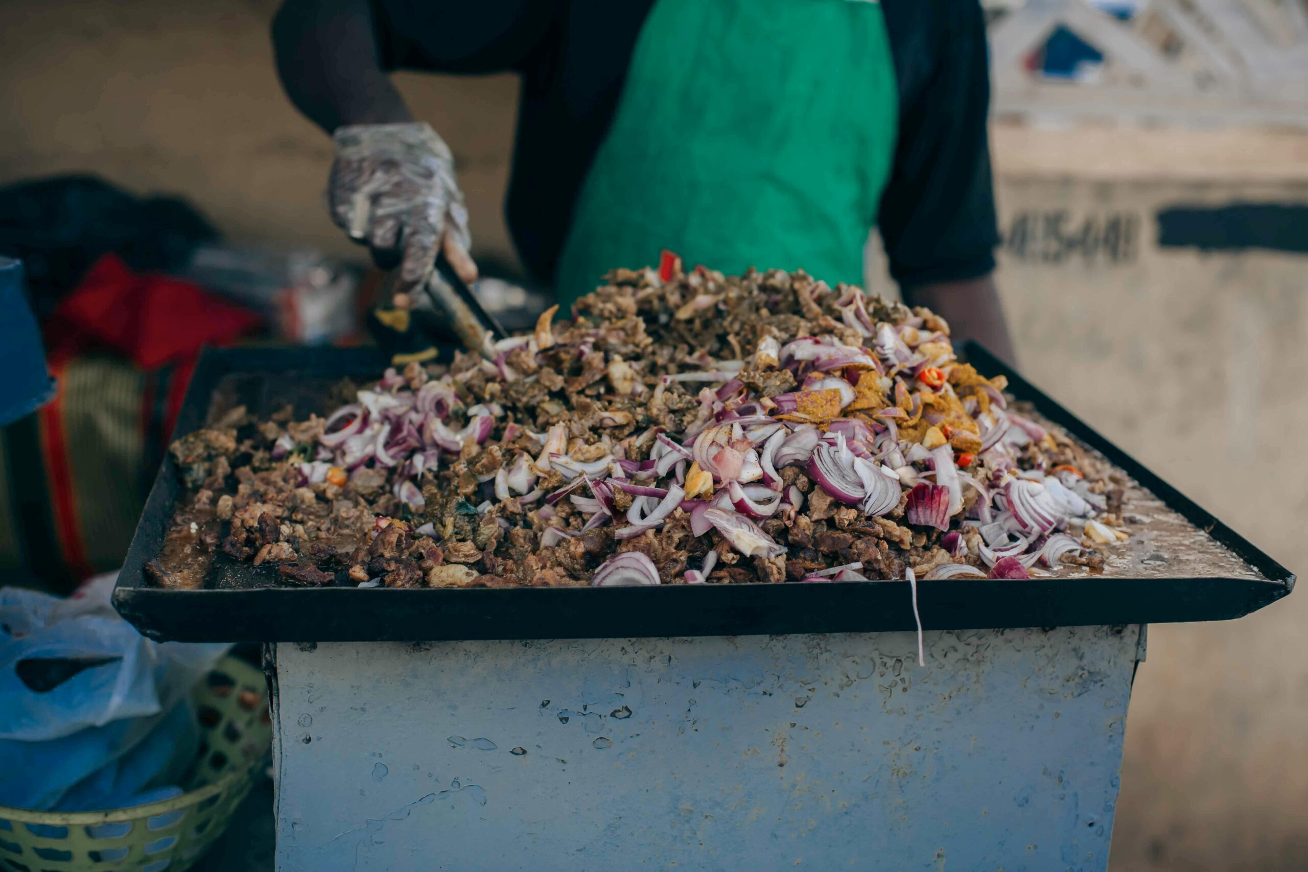 Street food vendor cooking a savory meat and onion dish on a griddle outdoors.